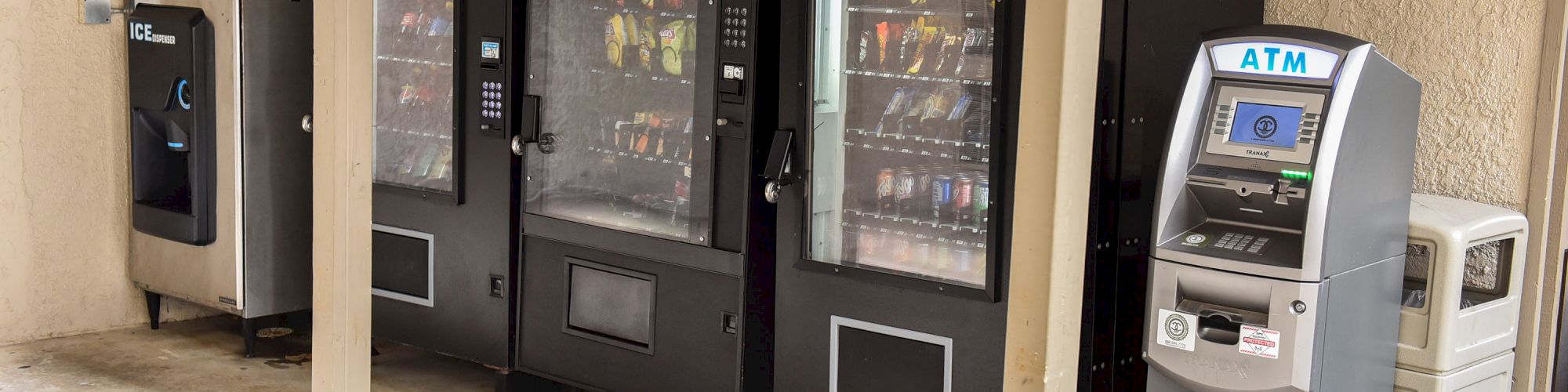 The image shows vending machines and an ATM next to a water dispenser and a trash can in an indoor area.