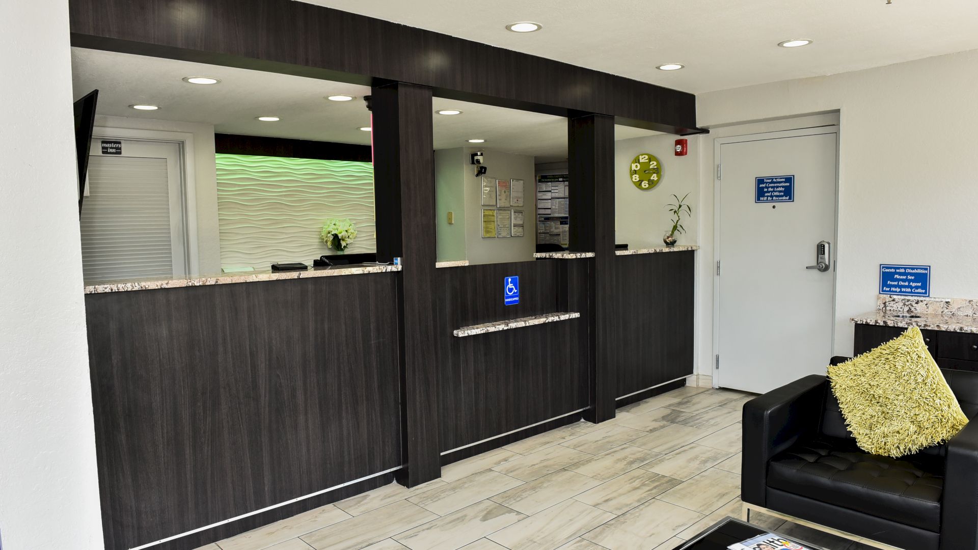 The image shows a modern reception area with a dark wood front desk, a black couch with a yellow cushion, and some wall decor.