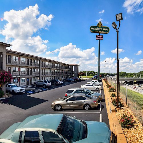 This image shows a roadside motel with parked cars and a highway adjacent to it under a partially cloudy sky.