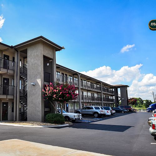 The image showcases a Masters Inn motel with multiple floors, exterior corridors, parked cars, and a clear blue sky in the background.