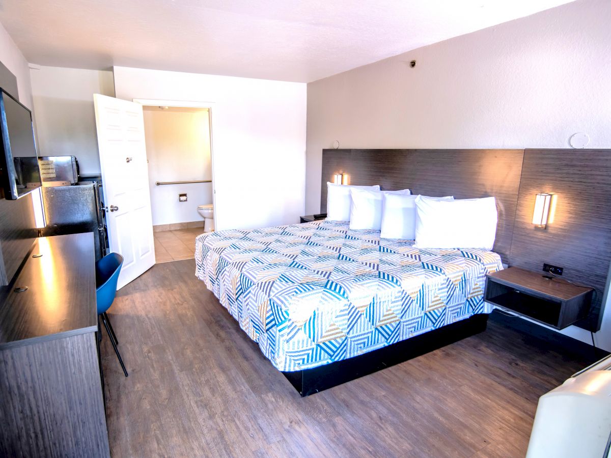 A hotel room with a modern design features a large bed, wall-mounted TV, desk, chair, and open bathroom door, all creating an inviting atmosphere.