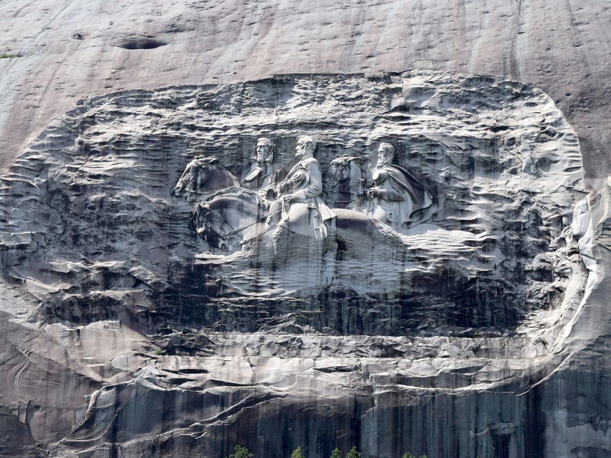 A massive rock carving depicts three historical figures on horses, intricately detailed on a stone mountain face.