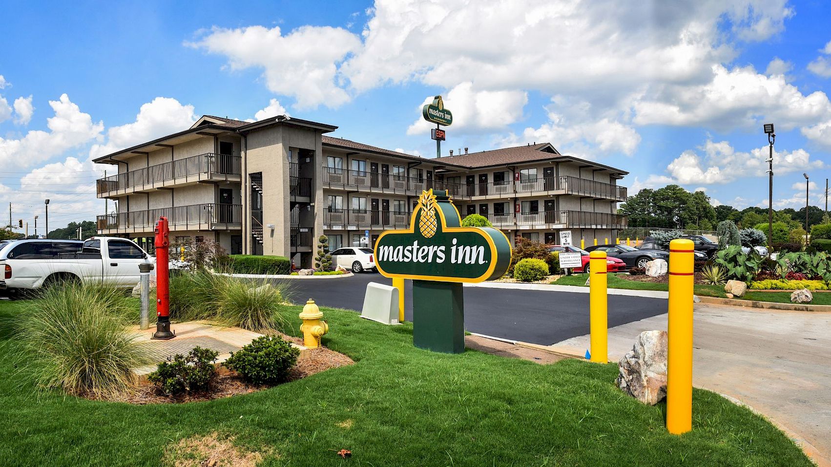 Image of a multi-story motel named "masters inn" with a parking lot, surrounding greenery, and blue skies with scattered clouds.
