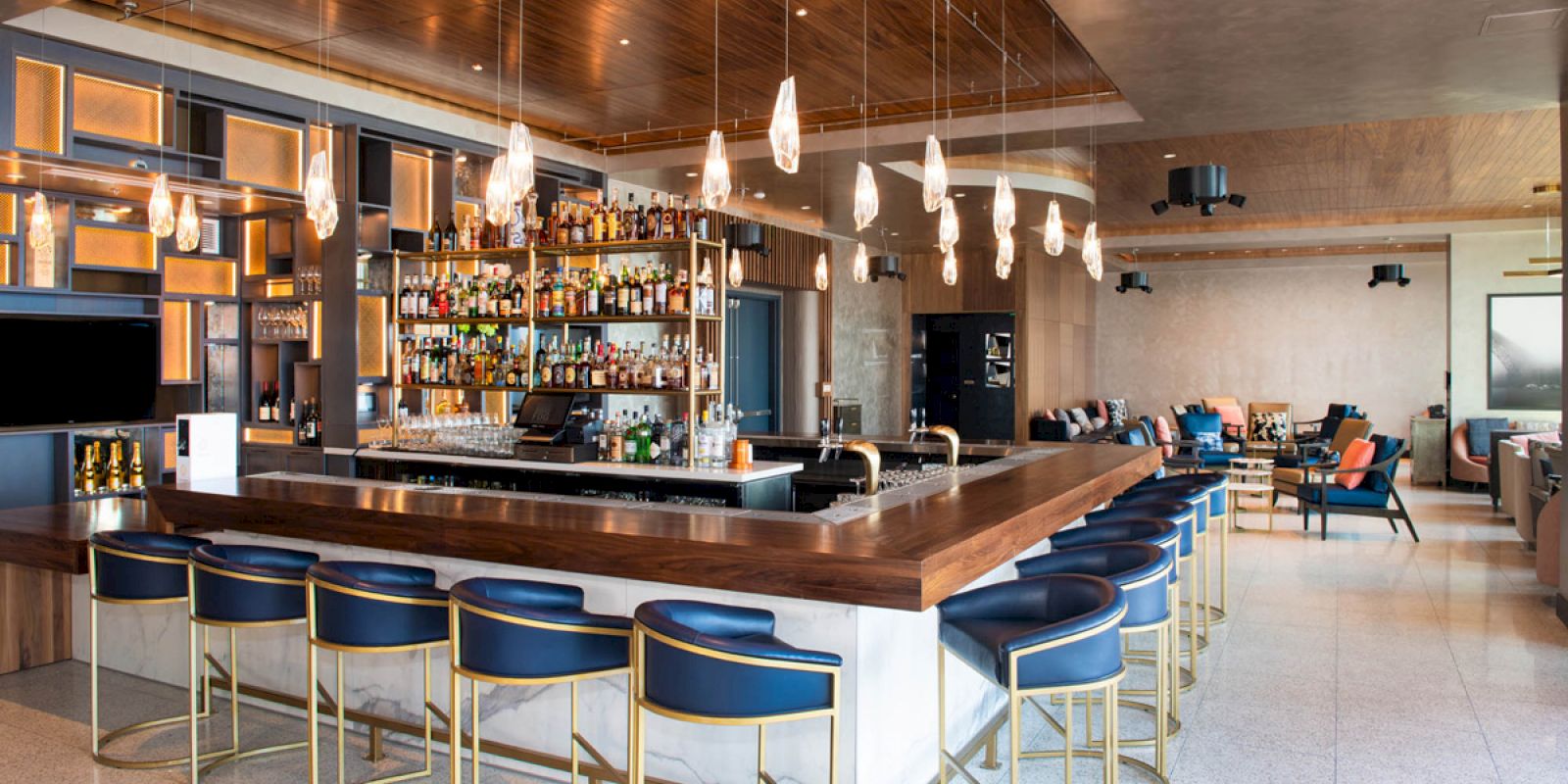 A modern bar with high stools, a well-stocked drink shelf, pendant lights, and a sleek design in a cozy lounge setting.