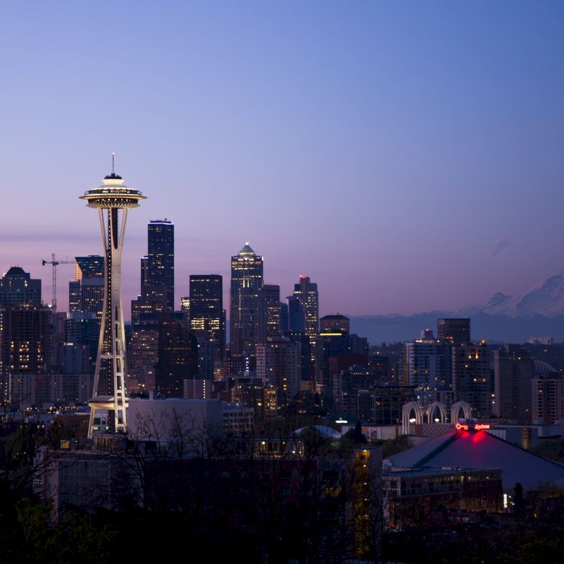 The image shows the Seattle skyline at dusk, featuring the Space Needle, various skyscrapers, and Mount Rainier in the background.