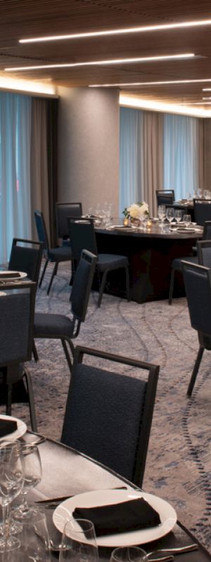 The image shows an elegant banquet hall set up with round tables decorated with white flowers, black napkins, and glassware, ready for a formal event.