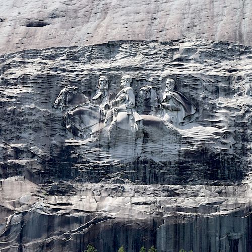 The image depicts a large stone carving featuring three figures on horseback etched into the face of a mountain.